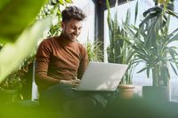 Un bărbat stă pe podea cu un laptop și lucrează la soluții durabile de digitalizare.