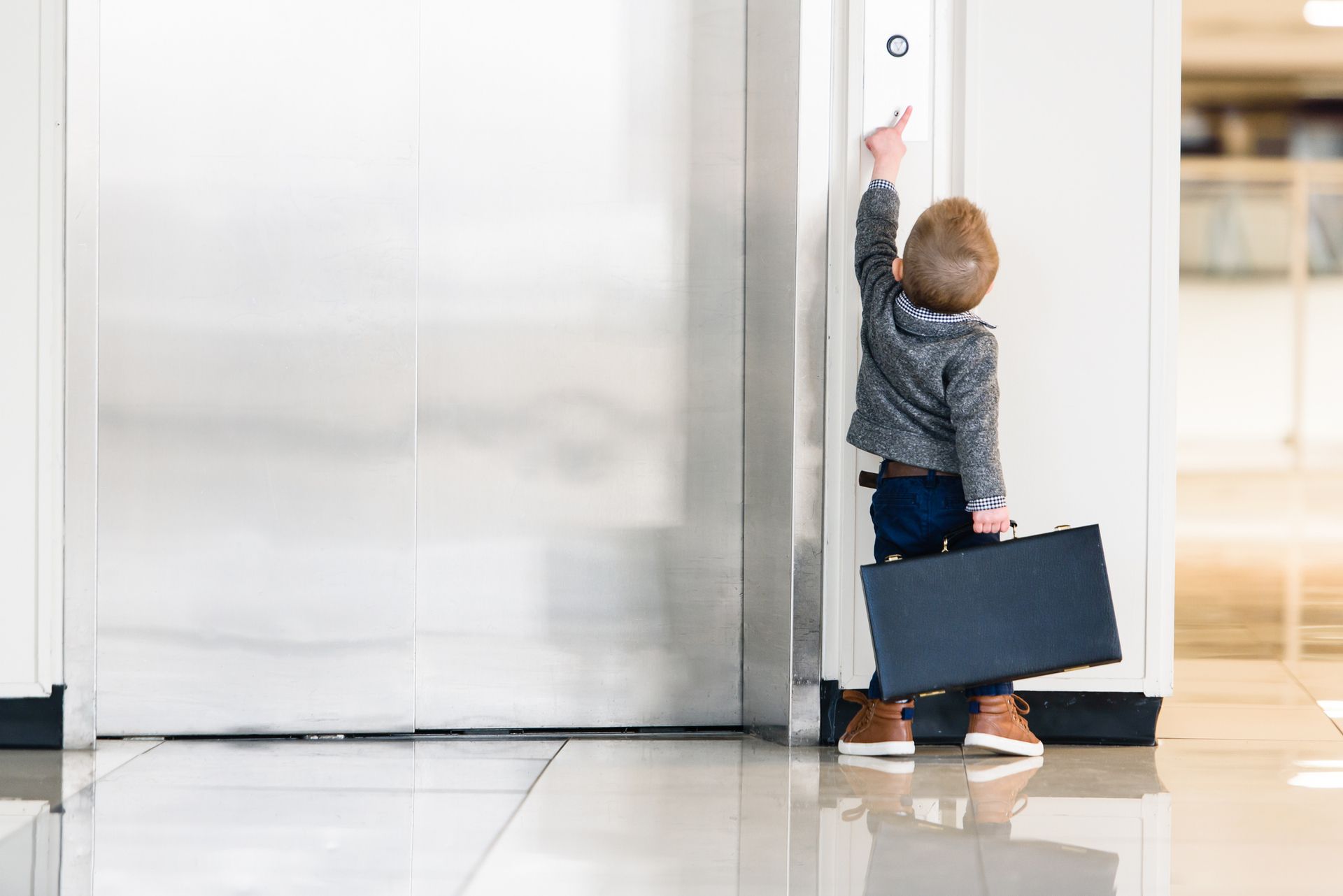 Copilul cu servieta arată spre un lift.