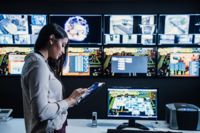 O femeie folosește o tabletă într-un centru de monitorizare cu mai multe monitoare.