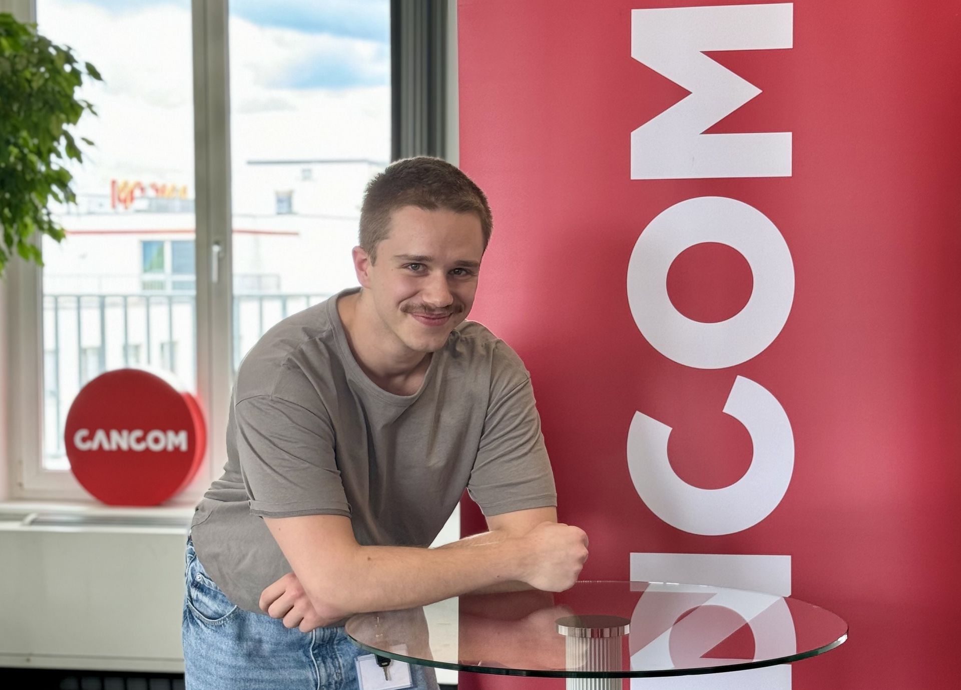 Bărbat în blugi sprijinit de o masă de sticlă, probabil într-o ședință sau în timpul unei pauze.