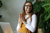 O femeie cu căști zâmbește în timp ce lucrează la un laptop, simbolizând serviciul clienți la CANCOM Austria.