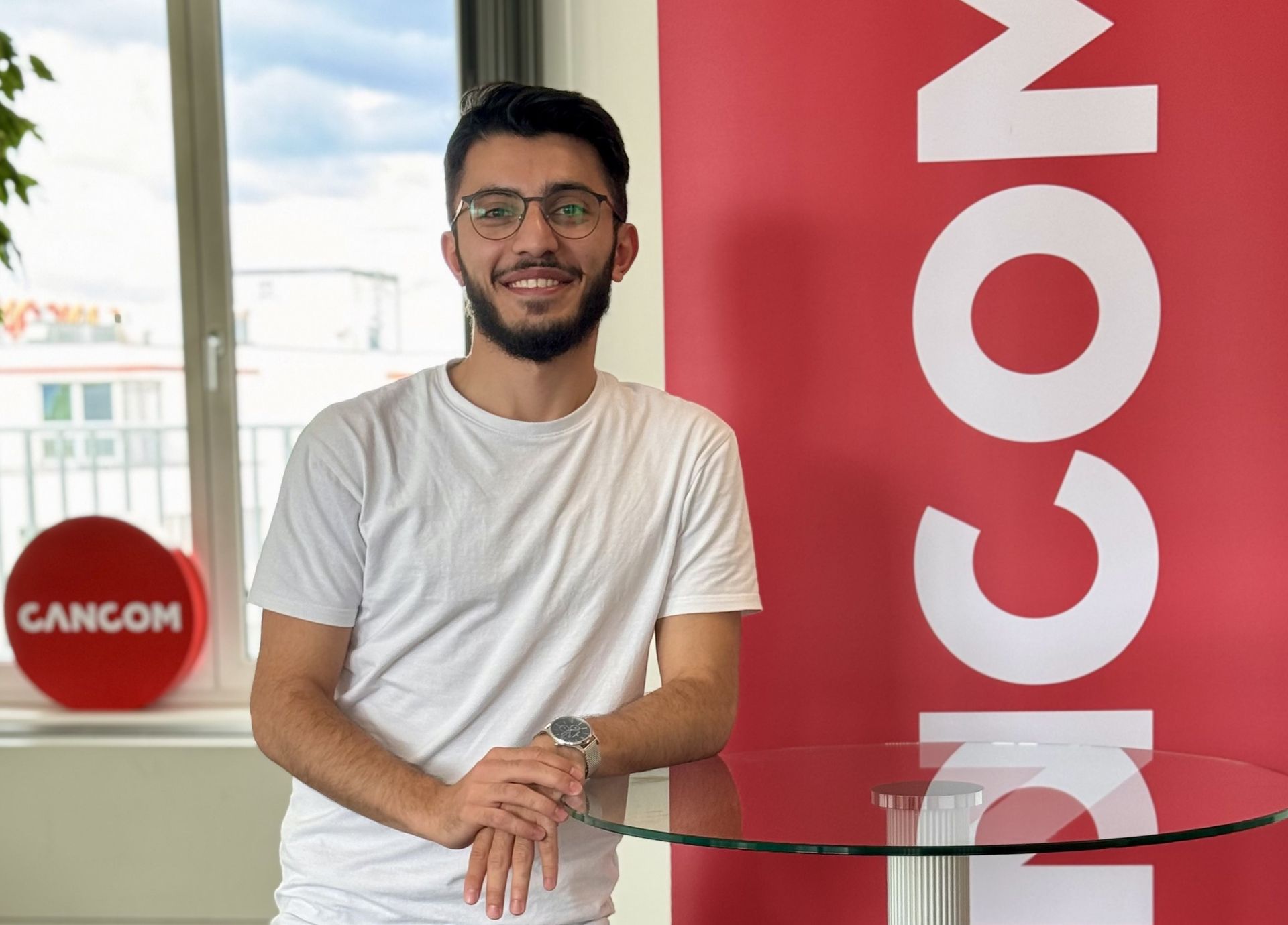 Bărbat cu ochelari și cămașă albă zâmbește în timp ce stă la o masă.